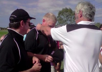 Coach Darren Nagle receives his Premiership medal from MVCC President Charlie Walker, who is also an NWCA junior official, while assistant coach Ross Aitken looks on.